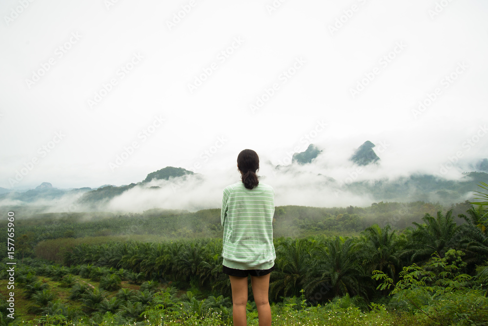 Lonely girl standing on the view point see tree forest and fog on the mountain background