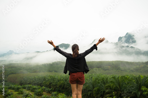 Girl standing on the view point see tree forest and fog on the mountain background