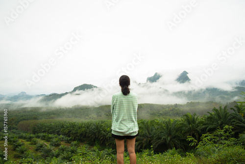 Lonely girl standing on the view point see tree forest and fog on the mountain background