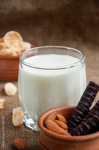 A glass of milk with almond nuts, corn flakes, chocolates, on sacking background