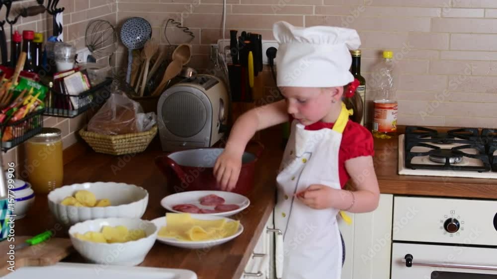 Cute small girl makes dinner. Small girl prepares food in the kitchen. Cute little girl dressed like a chef. Cute small girl makes dinner. Small girl prepares food in the kitchen. Cute little girl dressed like a chef.