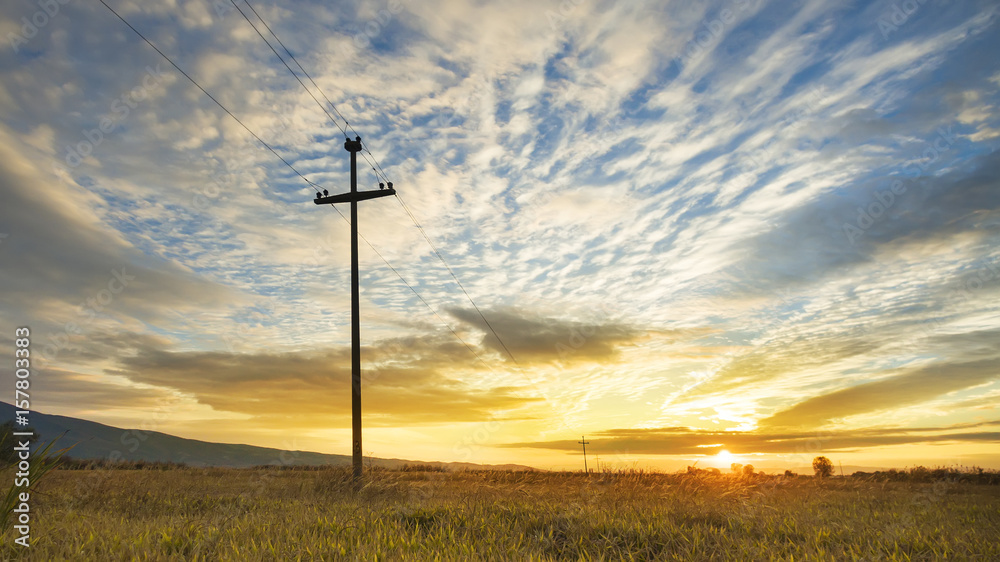 Electricity pole and harvest field on colorful sky, sunset