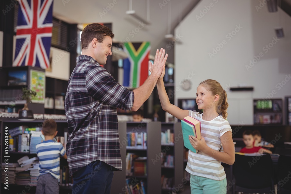Fototapeta premium Happy teacher and schoolgirl giving high five in library