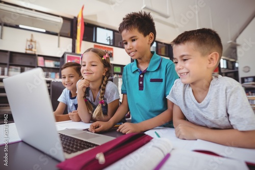 Cuadro en lienzo Happy schoolkids using laptop in library