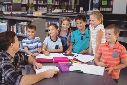Happy schoolkids interacting with teacher in library