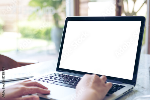 Mockup image of hand using laptop with blank white screen on vintage wooden table in cafe