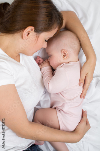 Mother and baby sleep in bed. Mom embraces her little daughter.