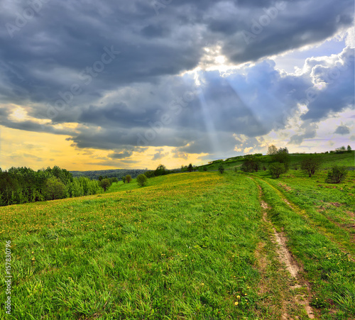 Foto Sun beams through clouds floating over the meadow