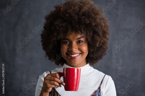 Photos Smiling woman with frizzy hair holding coffee mug against wall