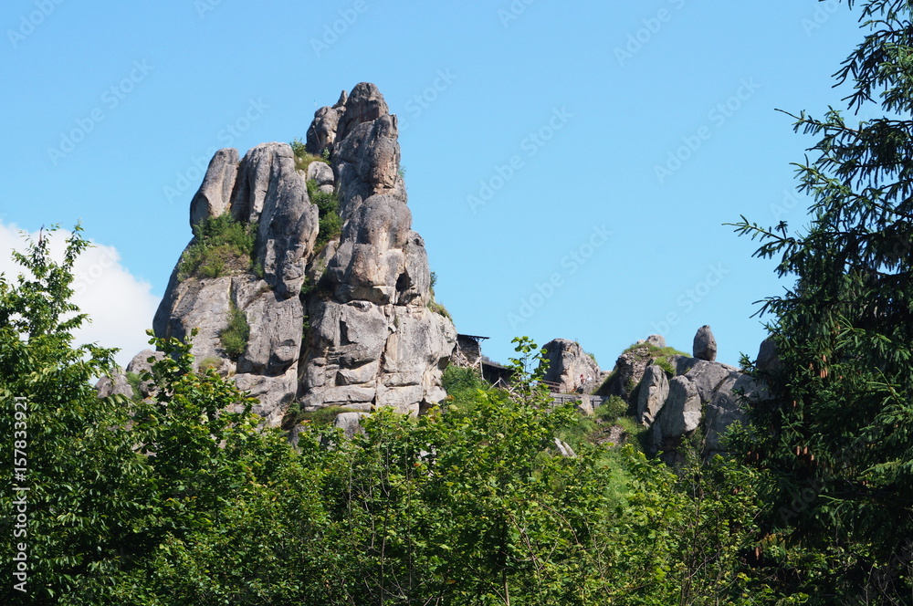 High stone rock in a green forest under a blue sky