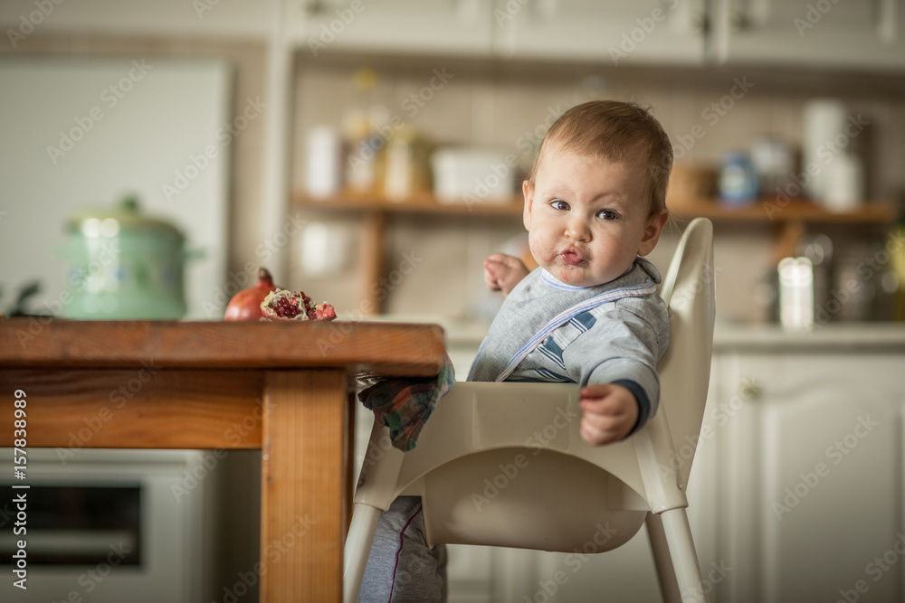 Portrait of blonde baby boy sitting at the dinner table eating pomegranate Portrait of blonde baby boy sitting at the dinner table eating pomegranate
