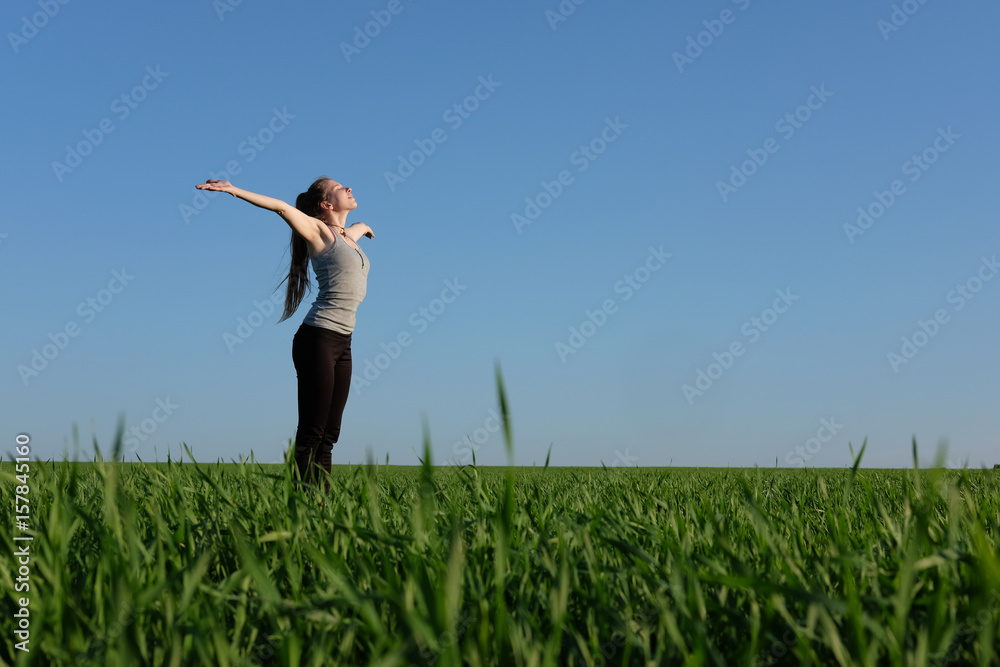 girl stretching herself in green field with blue sky background girl stretching herself in green field with blue sky background