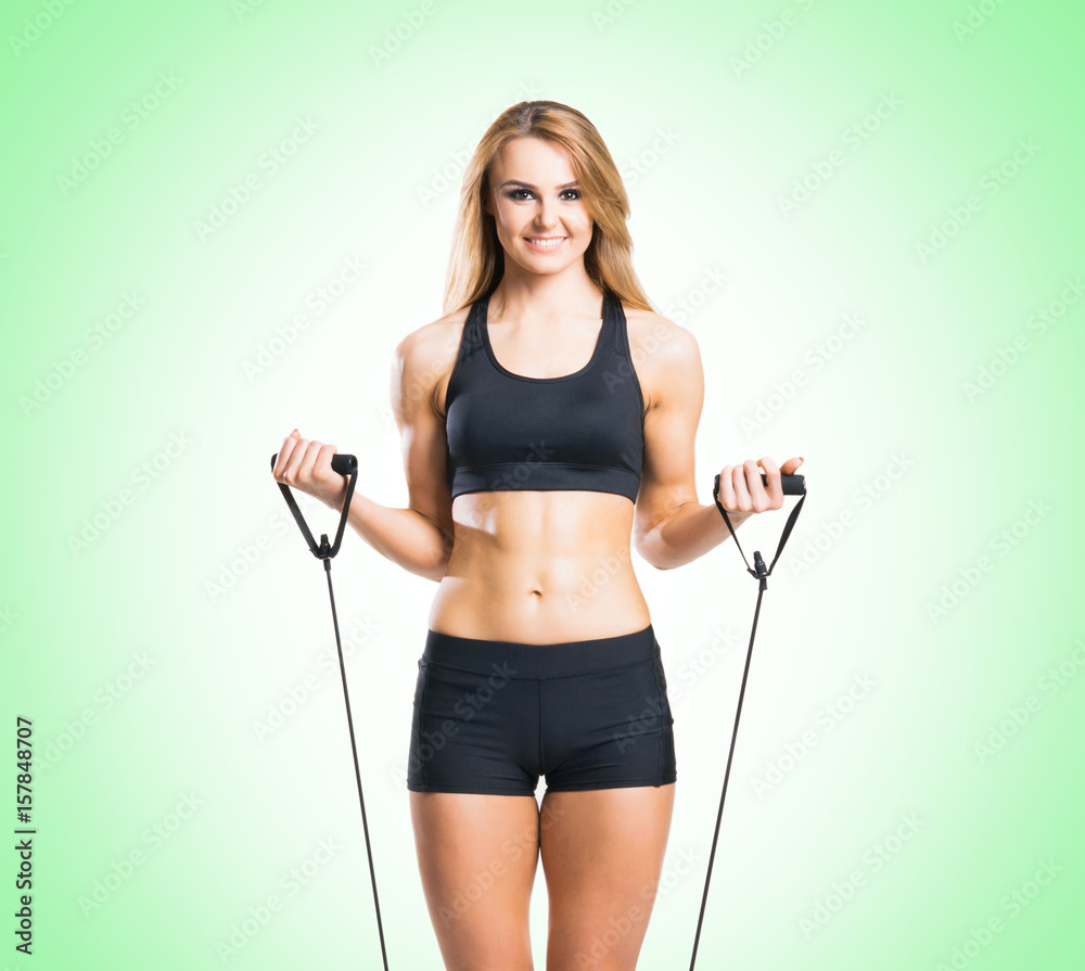 Fit, healthy and sporty woman in sportswear doing expander exercise green background.