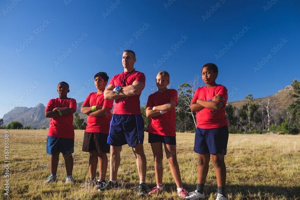 Trainer and kids standing with arms crossed in the boot camp