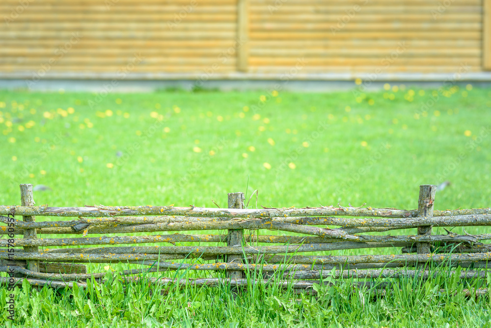 Fototapeta premium A braided wooden fence made of thin branches in the countryside against green lawn at the neat farm