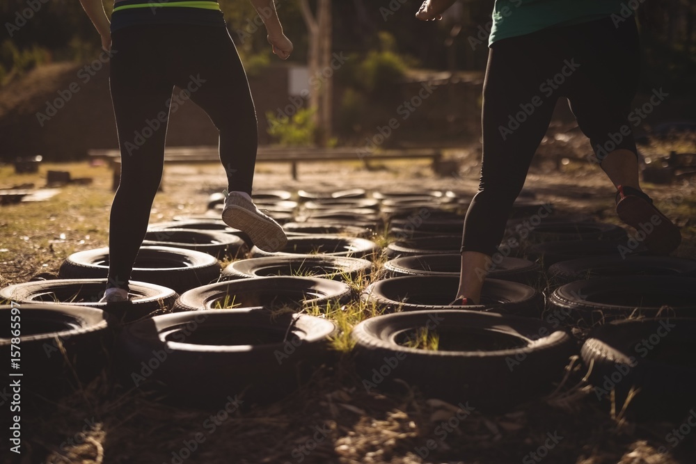 Low section of friends running over tires during obstacle course - obrazy, fototapety, plakaty 
