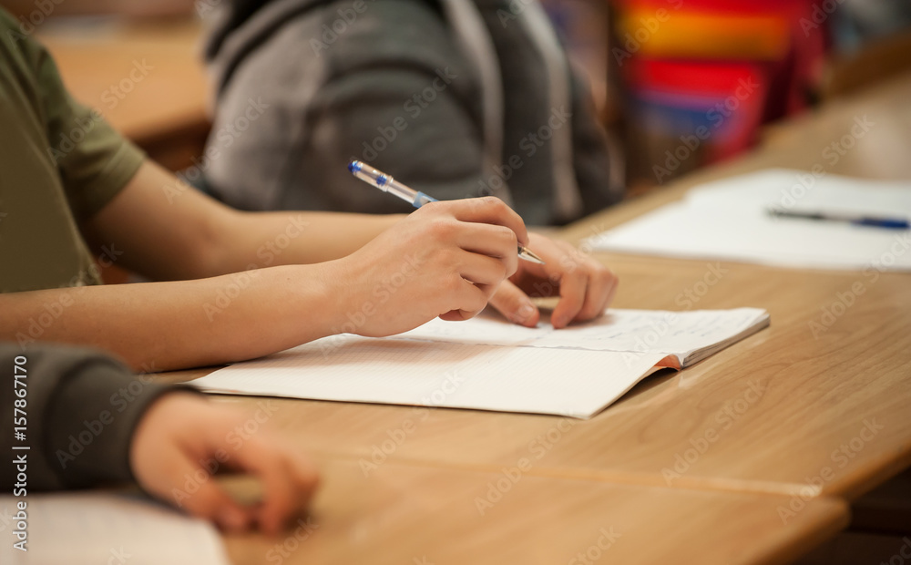 Closeup of student hands on school table writing to notebook Closeup of student hands on school table writing to notebook