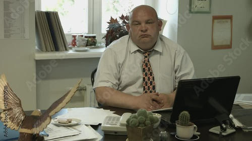 Ungraded: A bored fat bald office worker reluctantly pays attention to the visitor outside the frame, turns and looks straight to the camera.