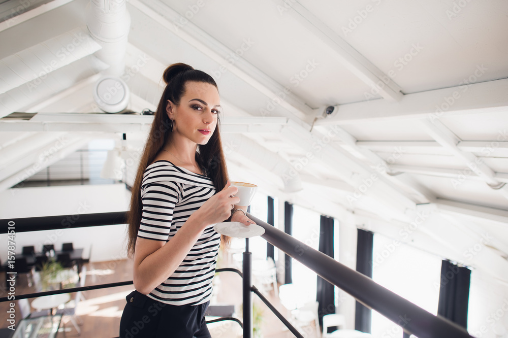 Close up portrait of a girl with brown hair holding take away coffee cup and smartphone while looking at the camera. Close up portrait of a girl with brown hair holding take away coffee cup and smartphone while looking at the camera.