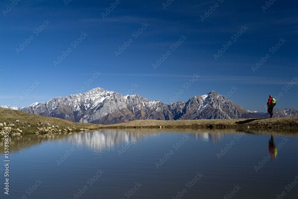 A hiker along the ridge of Mount San Primo reflected in a seasonal pond. From here the view stretches on Grignetta and Grignone. Bellagio. Lake Como. Lecco. Lombardy. Italy. Europe