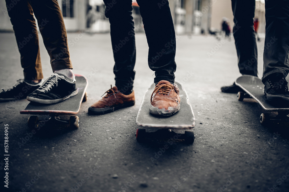 Fototapeta premium Group of friends skateboarders go in for sports on the street and ride skateboards, shoes in holes and abrasions. The concept is to lead the team to victory. Monochrome and high contrast.