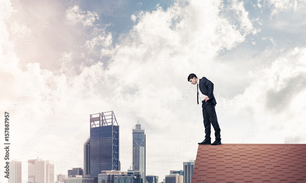 Businessman looking down from roof and afraid to make step. Mixe Businessman looking down from roof and afraid to make step. Mixe