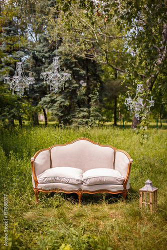Elegant white sofa in the garden, outdoor decorative composition with three chandeliers