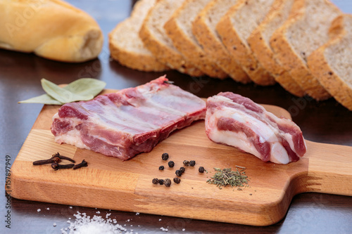 Raw pork ribs, salt, cloves, bay leaves, black pepper and thyme over a wooden cutting board, in front of wholegrain bread