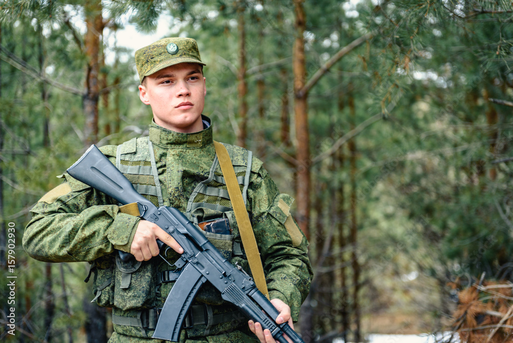Portrait of a Russian soldier in modern military uniforms and weapons, machine gun. Green form on the background of a pine forest