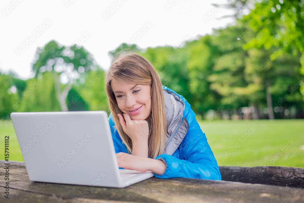 Smiling woman is working on a computer outdoors in the college park. Smiling woman is working on a computer outdoors in the college park.