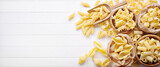 Raw pasta: pens, shells, rigatoni, fusilli and squid on white wooden background, top view, flat lay, copy space.
