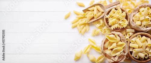Obraz  z motywem Raw pasta: pens, shells, rigatoni, fusilli and squid on white wooden background, top view, flat lay, copy space.