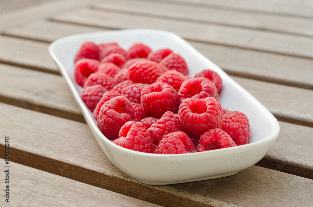 Fresh organic raspeberry on a white plate on a wooden table Fresh organic raspeberry on a white plate on a wooden table