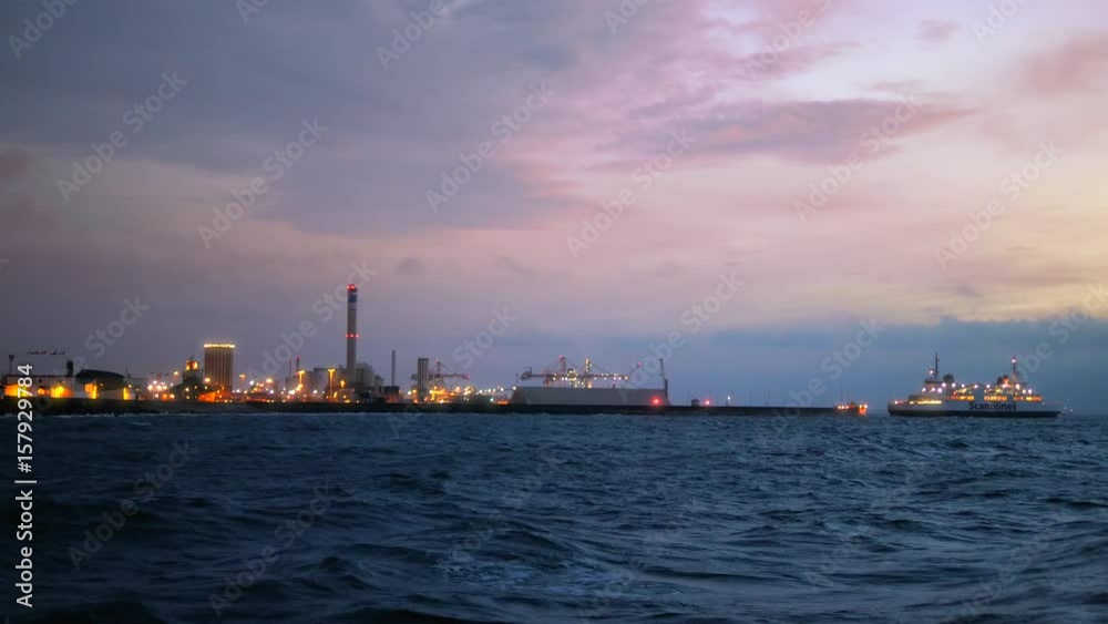Ferry boat arriving to harbor in Helsingborg, Sweden. Industrial buildings at dusk Ferry boat arriving to harbor in Helsingborg, Sweden. Industrial buildings at dusk