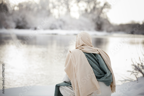Jesus Christ kneeling next to a river, pondering, in the snow. 