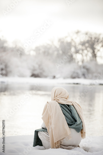 Jesus Christ pondering and kneeling next to a river in the snow. 