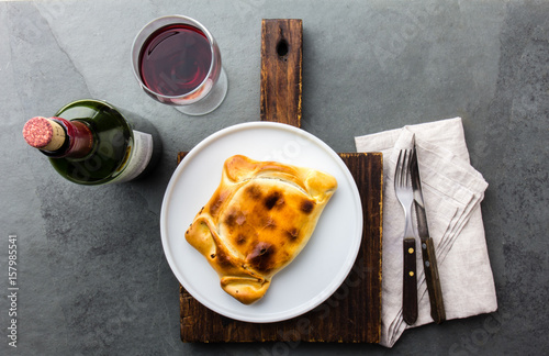 Chilean baked empanada de pino with meat, olives, onion and eggs served on wite plate with wine