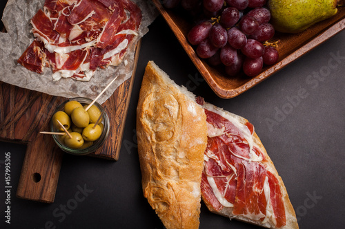 Jamon Iberico with white bread, olives on toothpicks and fruit on a dark background. Top view photo