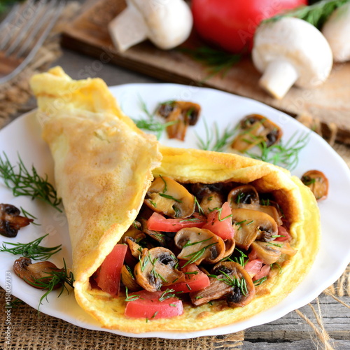 Vegetarian omelette idea. Fried mushrooms omelette with tomatoes and dill on a plate. Fresh mushrooms, tomatoes, dill on a vintage wooden background. Easy egg omelette. Rustic style. Healthy food