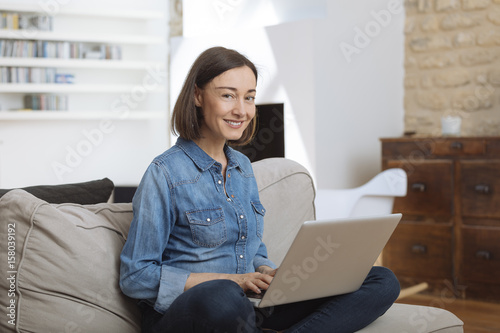 Attractive mature woman using a laptop while relaxing on a sofa at home