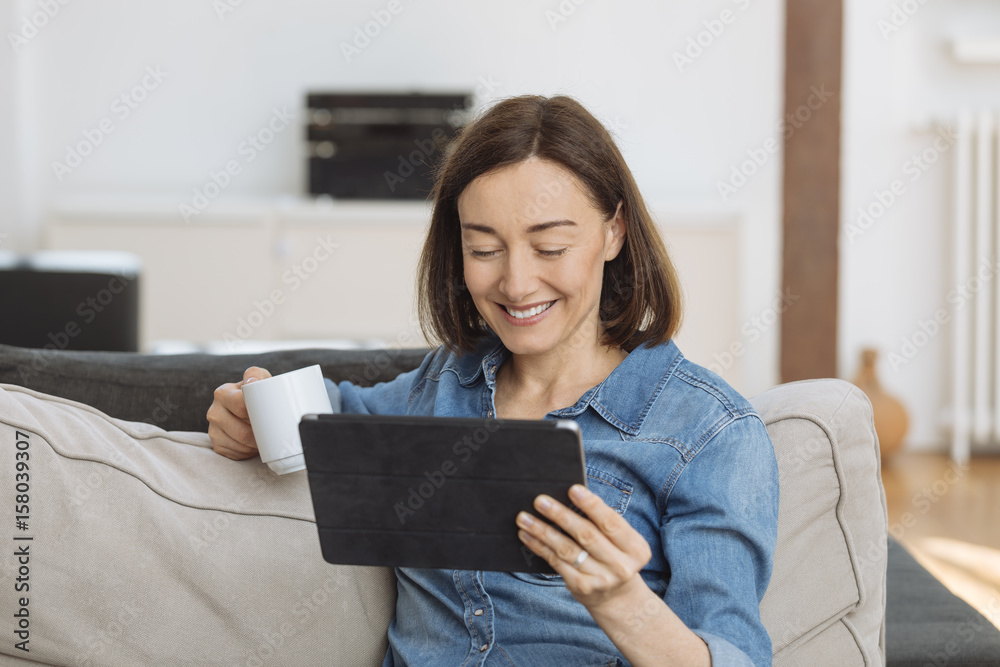 Mature woman using tablet computer while relaxing on sofa at home Mature woman using tablet computer while relaxing on sofa at home