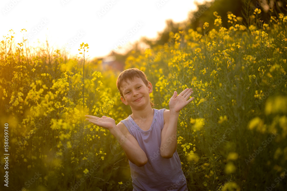 Naklejka premium Boy on a yellow rapeseed field in the evening at sunset