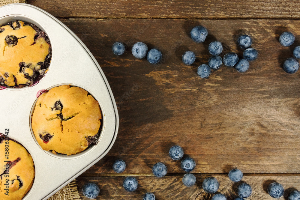 Freshly baked muffins and blueberries on rustic texture Freshly baked muffins and blueberries on rustic texture