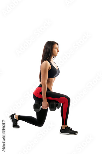 A slender athletic woman shows a dumbbell exercise in the hands of a dumbbell, a right foot in front, a full squat position, on a white background.