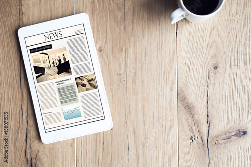 Newspaper on digital tablet on wooden table