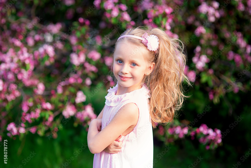 Fototapeta premium Beautiful smiling cute girl with long curly hair in blooming pink apples