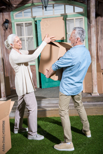 Smiling senior couple holding cardboard boxes while moving into new house
