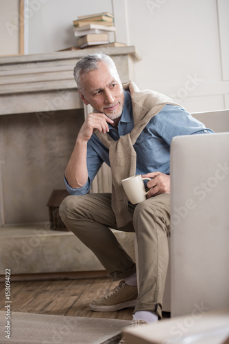 pensive senior man with coffee cup looking away