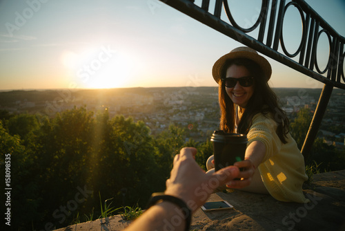Tablou pe pânză Female giving coffee to man while they sitting on the hill on sunrise