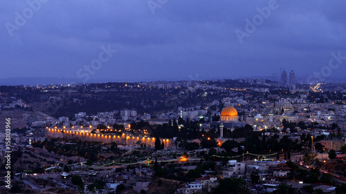 Night falls on Jerusalem city. Citylights light up at night while sunset goes over Jerusalem Dome of the Rock and Al Aqsa mosque.
